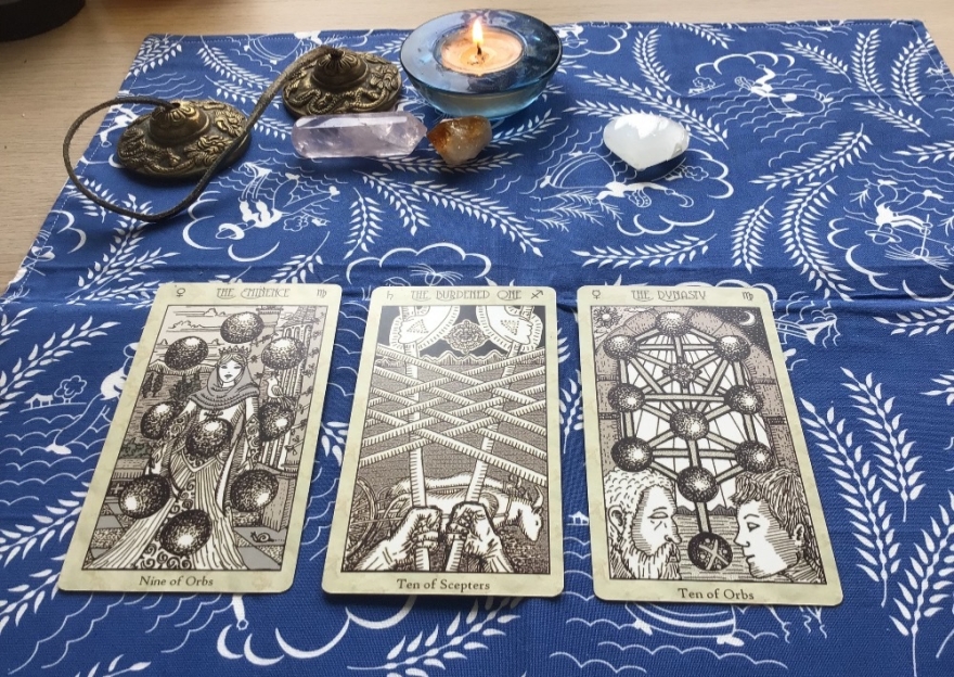 3 tarot cards on a tarot cloth and a candle and some crystals